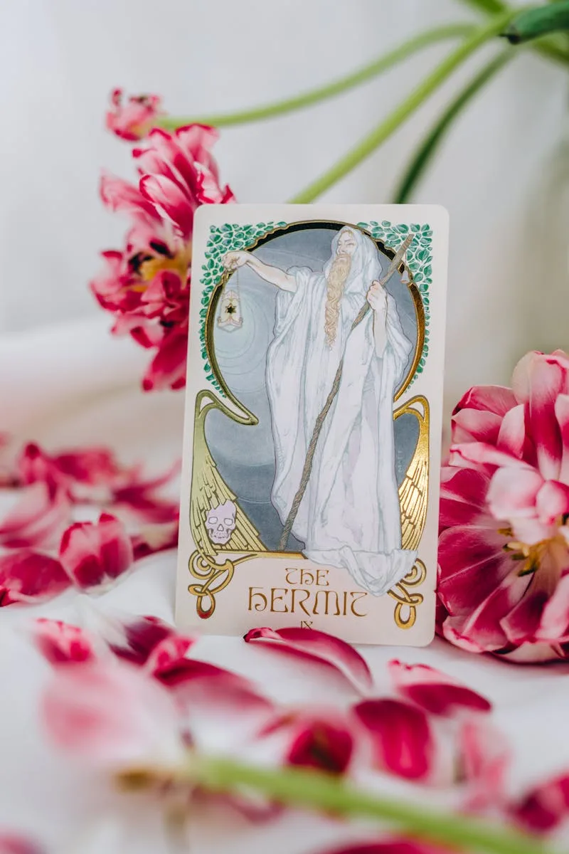 The Hermit tarot card surrounded by vivid pink flowers, symbolizing introspection and guidance.