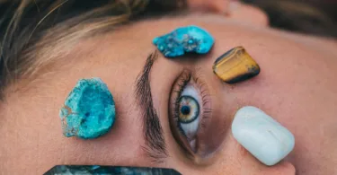 Close-up of a person's eye surrounded by vibrant healing stones on skin for relaxation therapy.